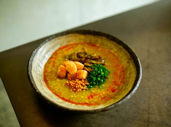 A bowl of congee with an orange hue, adorned with toppings.