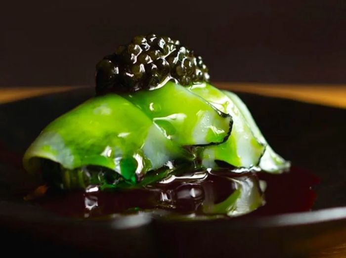 A translucent, vibrant green slice of fish rests atop dark rice, finished with a dollop of caviar.