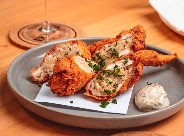 Four chicken wings, filled with a flavorful ground mixture and garnished with chives, served alongside a glass of wine.