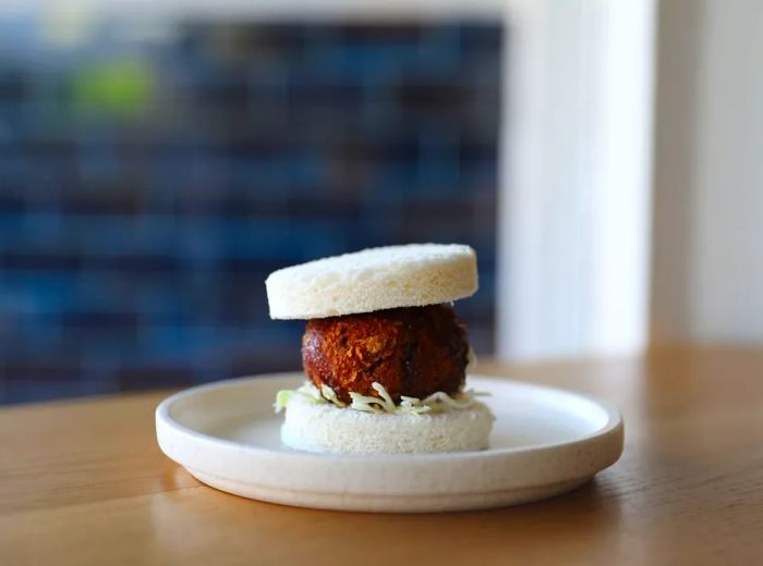 A katsu patty resembling a meatball nestled between slices of soft, crustless white bread.