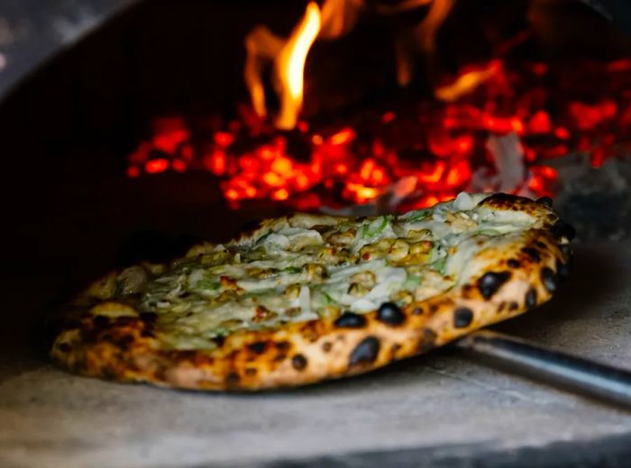 A white pizza is placed into a dark wood-fired oven.