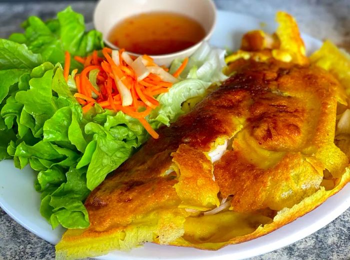 Bánh xèo accompanied by fresh salad and a dipping sauce.