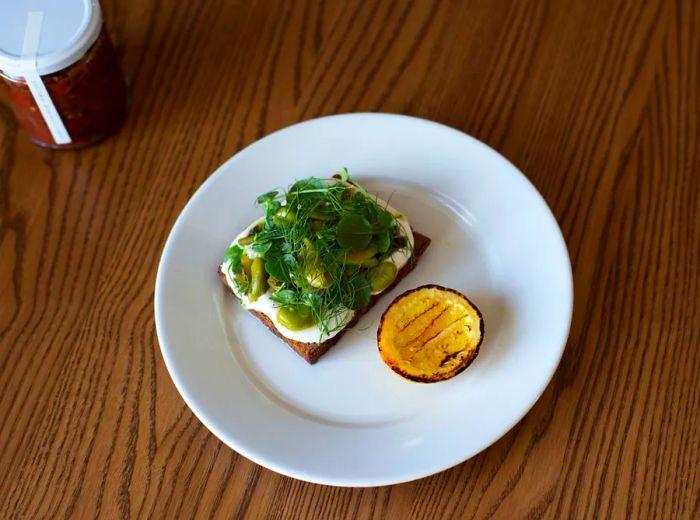 A toast topped with a creamy bean and feta mash, garnished with greens and served alongside a charred lemon wedge.