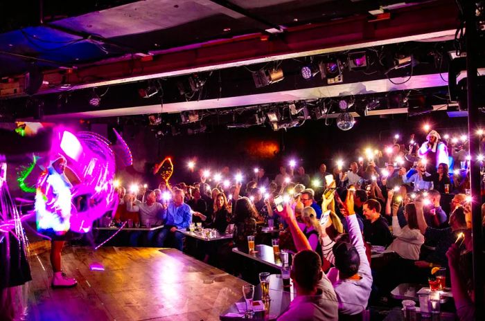 Brittani Yawn and Claudia Martinez shine in reflective outfits as audience members illuminate the room with their cell phone lights at Second City, Chicago.