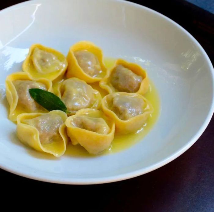 Plump, stuffed pasta served in a bowl of broth, garnished with a fresh basil leaf.