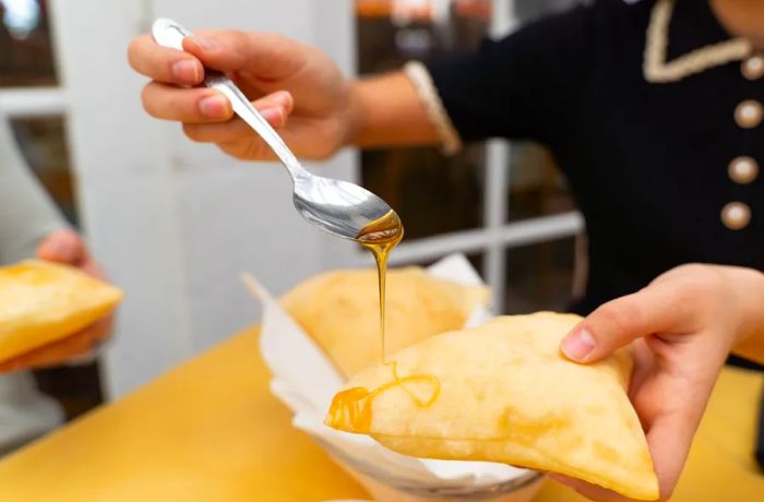 A diner drizzles honey onto the edge of a sopaipilla.