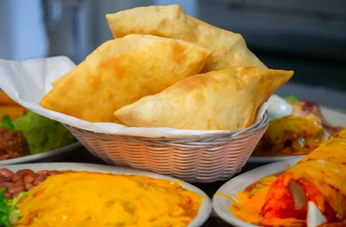 A basket filled with sopaipillas, accompanied by other New Mexican dishes.