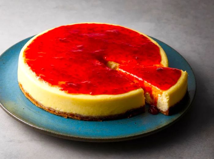 A vibrant cheesecake topped with a bright red glaze, with a slice slightly pulled out.