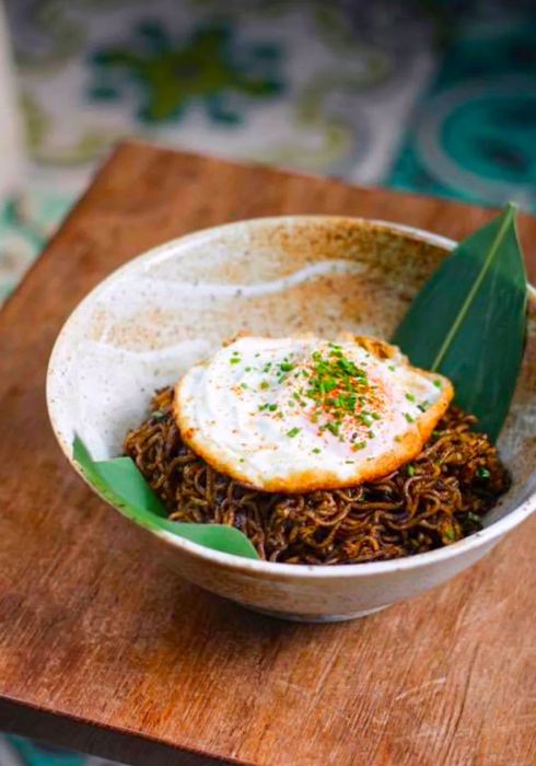 A bowl of maggie goreng topped with a herb-dusted fried egg.