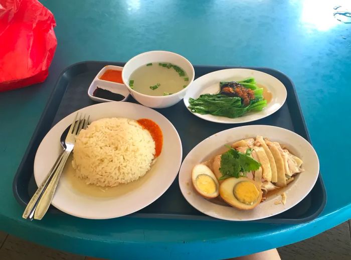 A tray displaying all the elements of Hainanese chicken rice arranged in separate dishes.