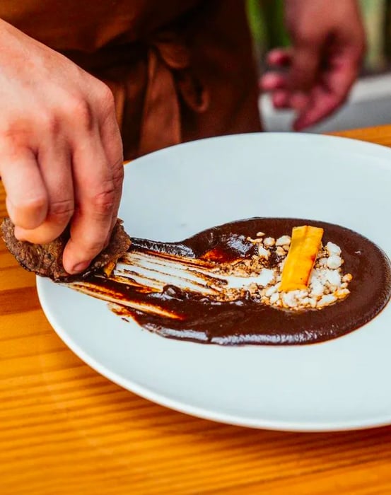 A hand scoops up a pool of mole using a tortilla.