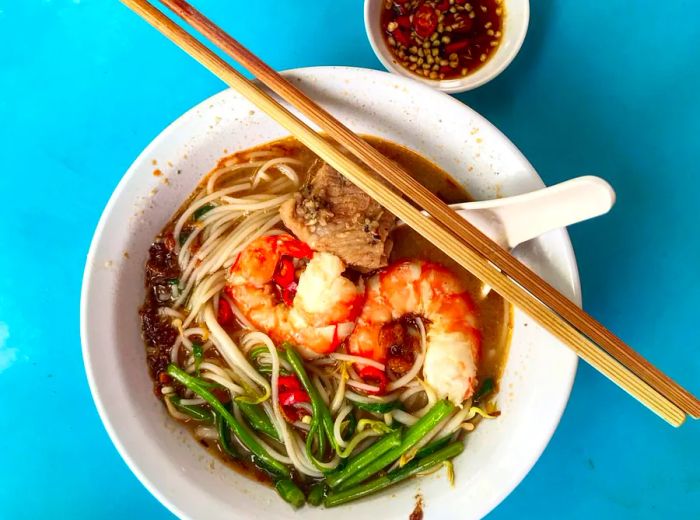 An overhead view of a bowl of prawn me against a blue background.