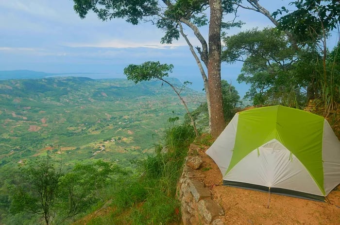 A tent positioned on the brink of an escarpment, offering scenic rural hills that stretch towards a distant lake.