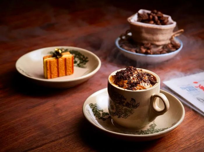 A dish served in a traditional kopitiam-style mug, with other dishes visible in the background.