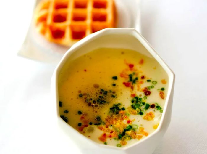 A bowl of soup accompanied by a waffle.