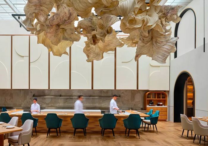 A spacious, airy restaurant where chefs work behind a central counter, all beneath a large and elaborate mobile art piece.