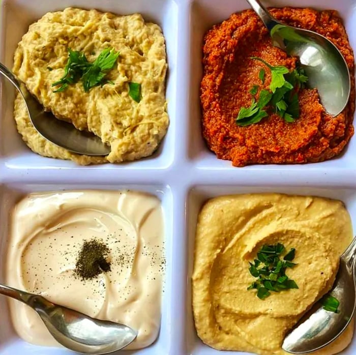 A segmented plate showcases four dips, each adorned with a unique herbal or spicy topping, as seen from above.