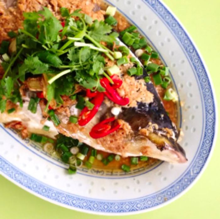 A closeup view of a whole fish topped with an abundance of herbs and chilies.