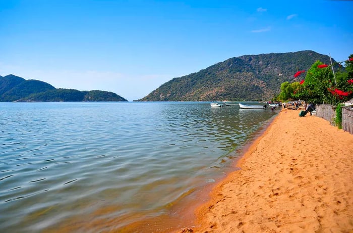 A stretch of golden sand gently kissed by the lake, with boats anchored in the distance.