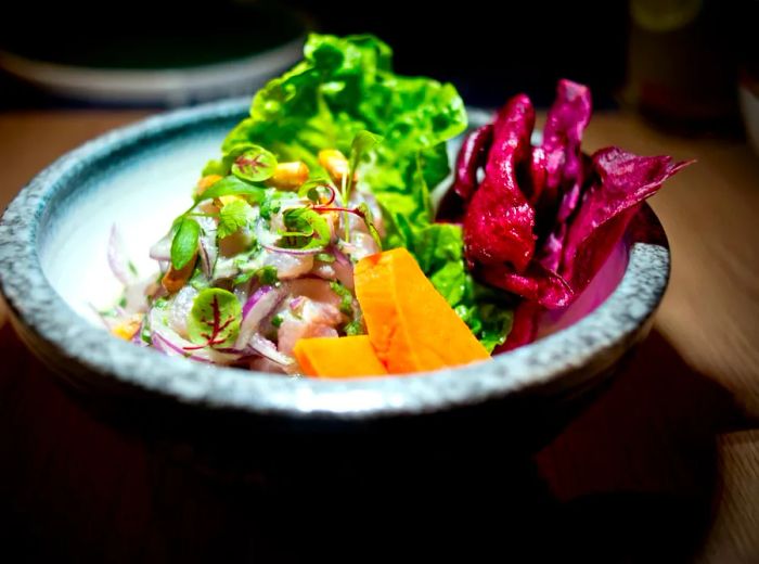 A vibrant bowl of ceviche featuring sweet potato, fresh vegetables, and crunchy corn nuts.