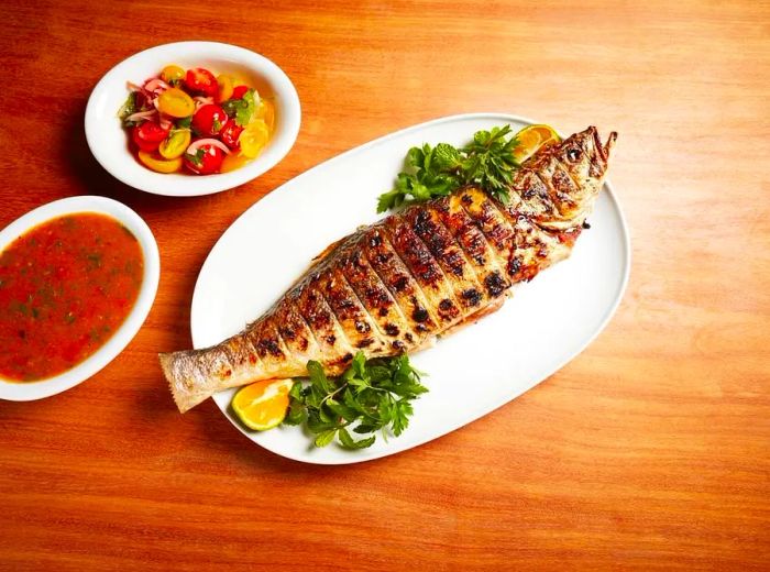 A beautifully roasted whole fish accompanied by various side dishes.