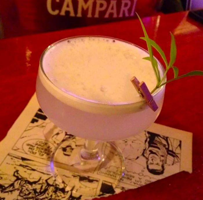 A creamy cocktail, garnished with a sprig of herbs secured to the rim with a tiny clothespin.