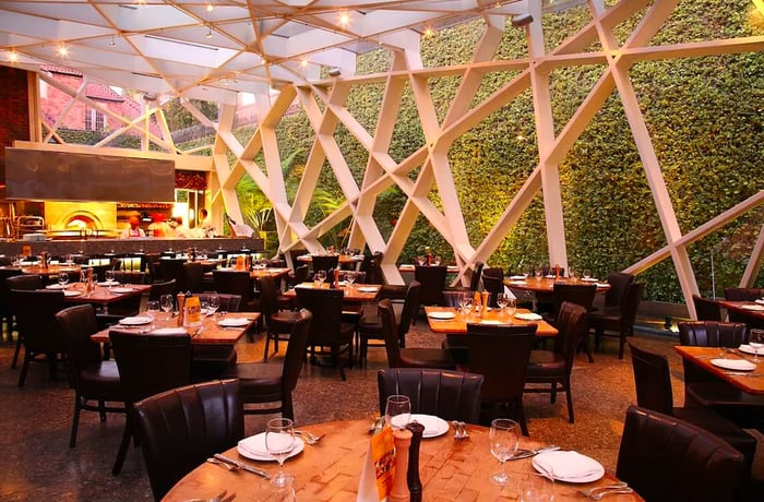 Tables arranged under a striking open-air glass structure.