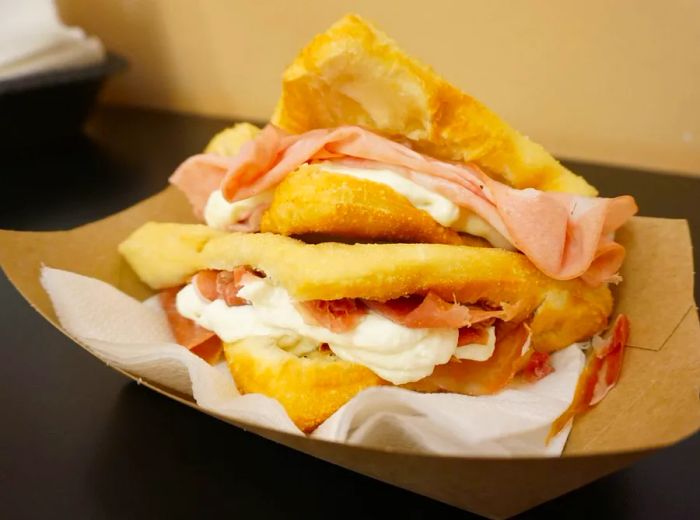 Two towering sandwiches overflowing with meat and cheese, presented in a paper boat.