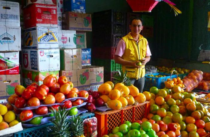 A vendor surveys a colorful display of fruit stacks.