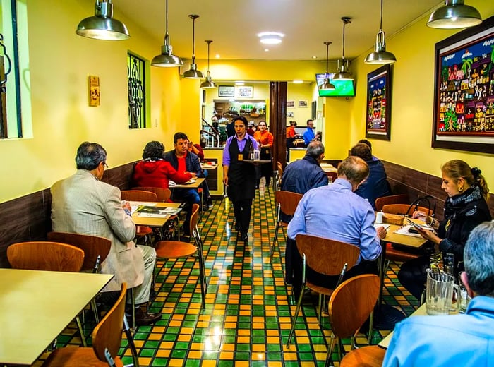 A server navigates through a lively dining area featuring striking green and yellow tiled floors.