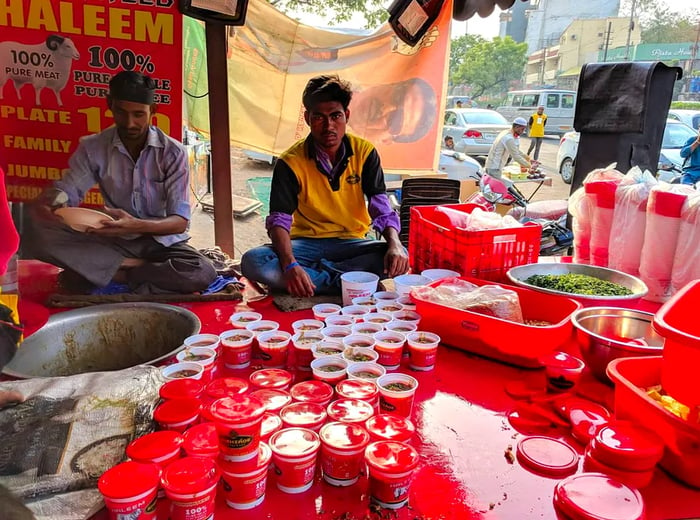 Workers surrounded by a variety of bowls of haleem next to their cooking pot.