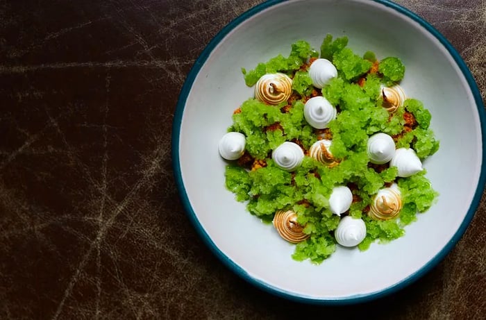 An overhead view of a dish featuring meringue-like puffs resting on a bed of green shavings.