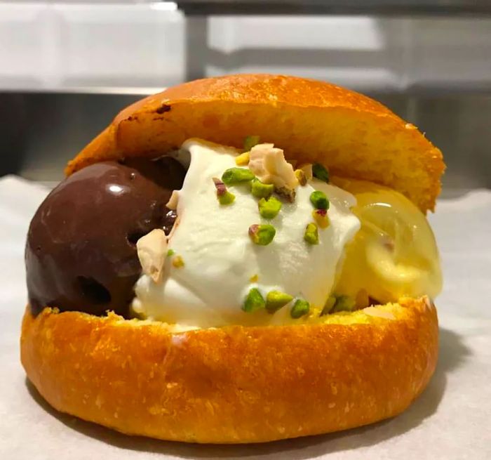 An ice cream sandwich filled with three flavors, featuring glossy chocolate and one sprinkled with chopped pistachios.