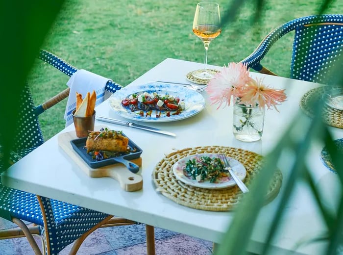 a glimpse through palm leaves at a dining setup adorned with wine and dishes.