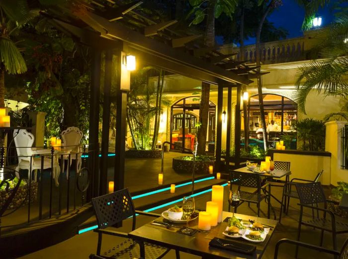 Tables adorned with candles on a covered patio surrounded by greenery at night.