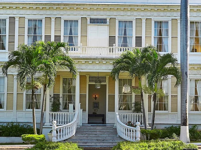 An elegant mansion entrance bordered by swaying palm trees.