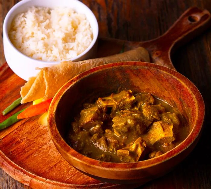 A bowl of green stew placed on a table next to rice.