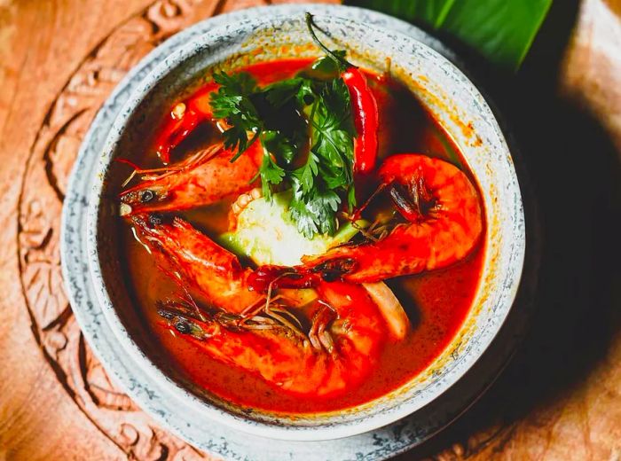 A bowl filled with large, head-on shrimp swimming in a vibrant red broth.