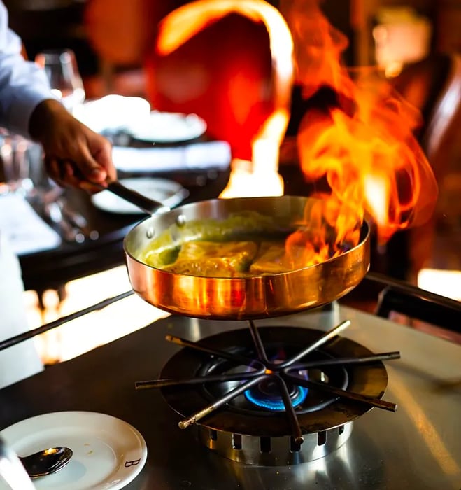 A chef performs flambéing at the table for guests.