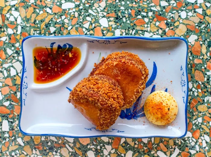 An aerial view of two prawn toasts topped with crushed nuts, accompanied by a dipping sauce.