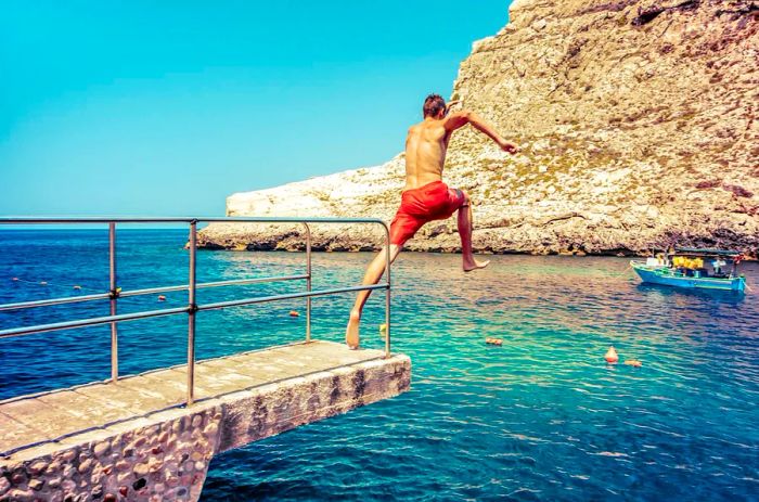 A young man leaps from a walkway into the sea at Xlendi Beach on Gozo, Malta.