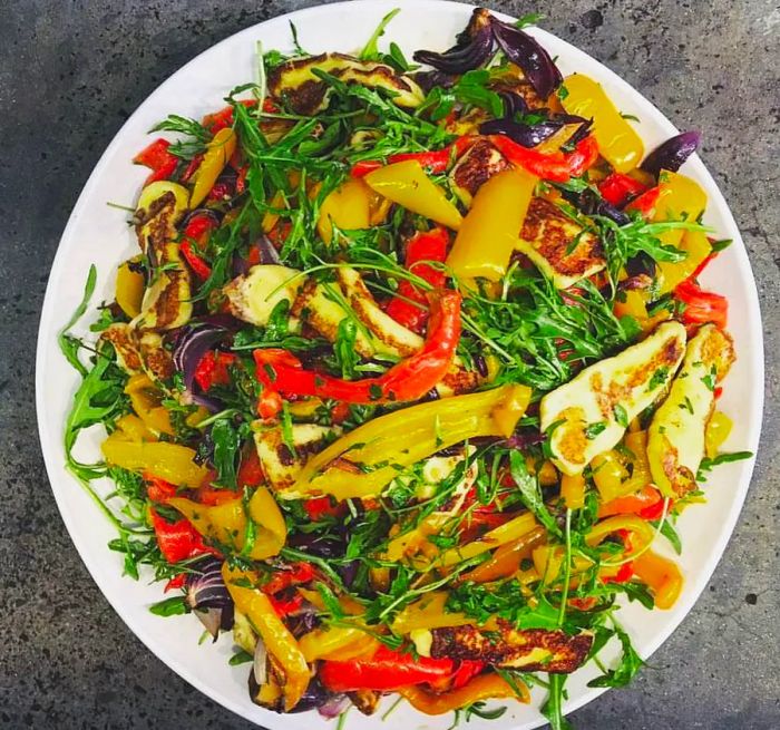 An overhead view of a salad plate adorned with shreds of peppers, red onion, and halloumi cheese.