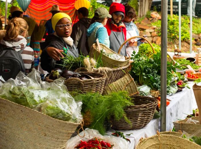 Shoppers sift through abundant wicker baskets filled with vibrant vegetables and fresh herbs.