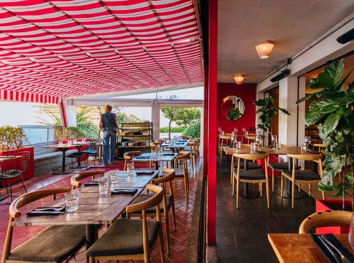 An image capturing two restaurant areas: one indoors and another on the patio, where a server is setting the tables.