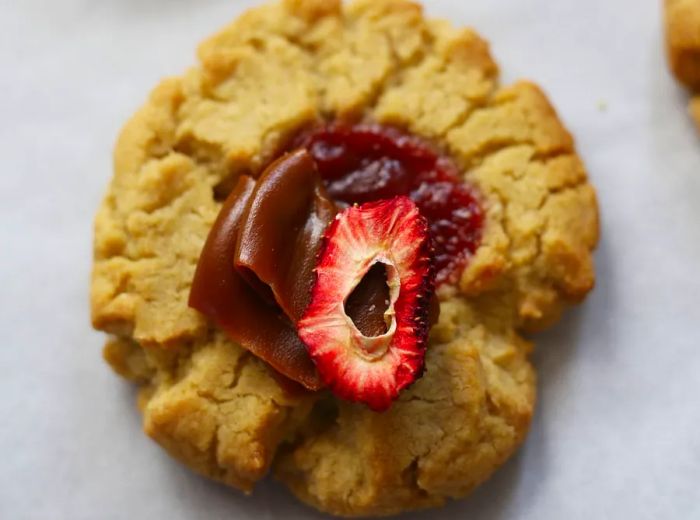 A detailed view of a cookie garnished with jam, a slice of dehydrated strawberry, and caramel.