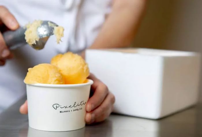 A staff member scoops a vibrant yellow ice cream into a cup.