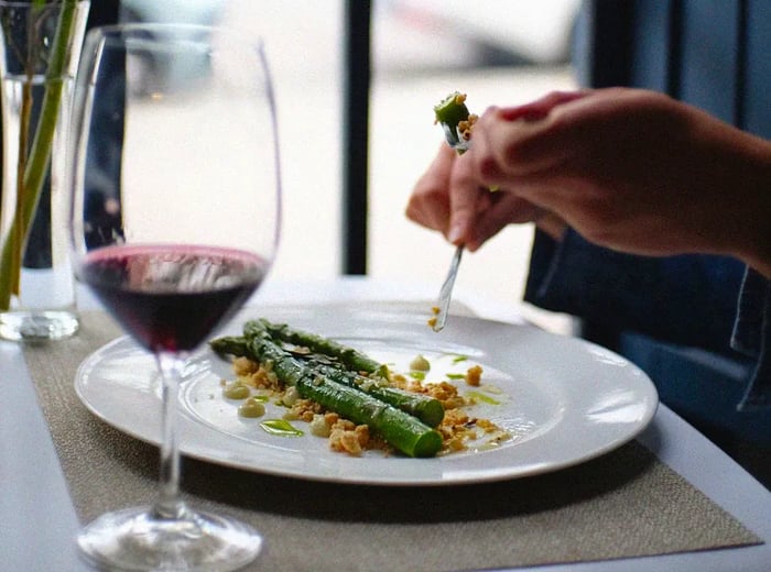 A diner enjoys a plate of asparagus paired with a glass of red wine.