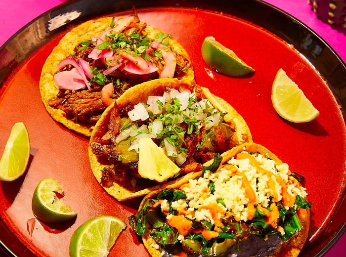 A tray featuring three tacos accompanied by lime wedges.