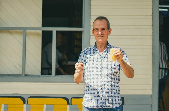 A man enjoys a glass of caldosa with a spoon outside a restaurant.