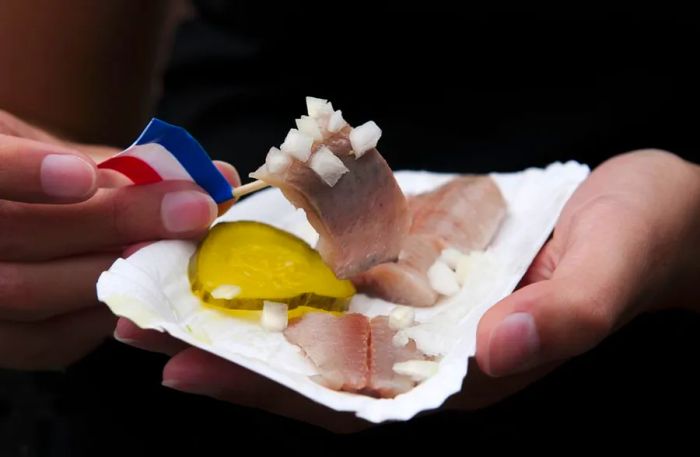 Pieces of herring are lifted with a toothpick by hands.